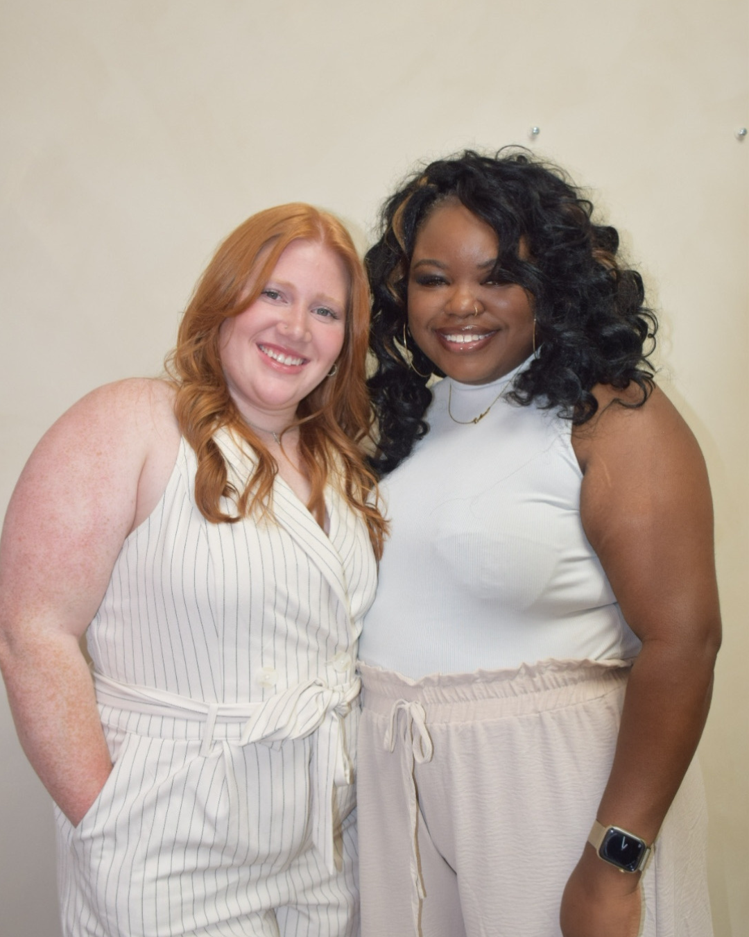 2 beauticians standing smiling for a photo hugging a poem dark skin and a lighter shade theme and have red hair